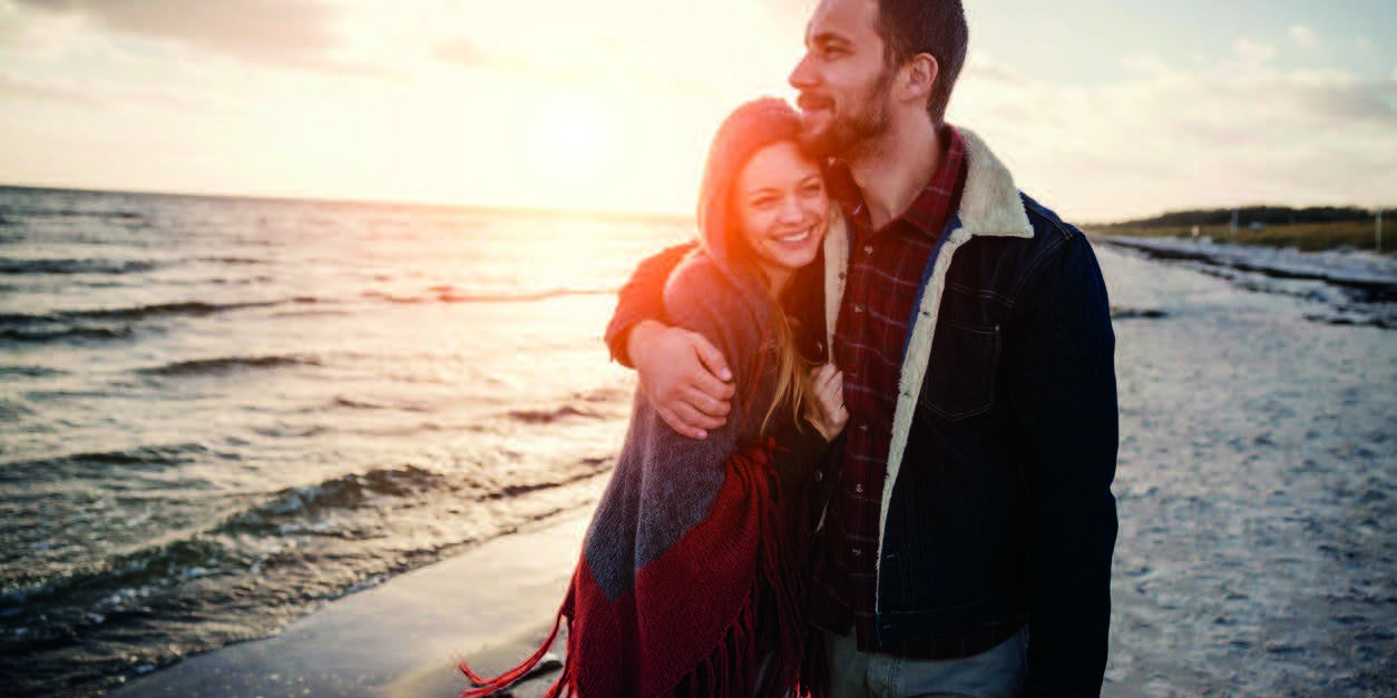 husband hugging smiling wife during walk on beach after recovery from mental health and substance use at Crossroads