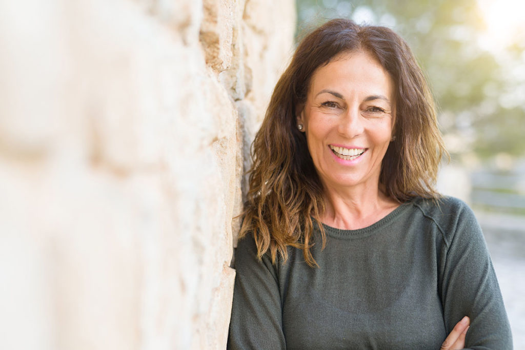 middle aged woman smiling next to rock wall because of benefits of residential treatment