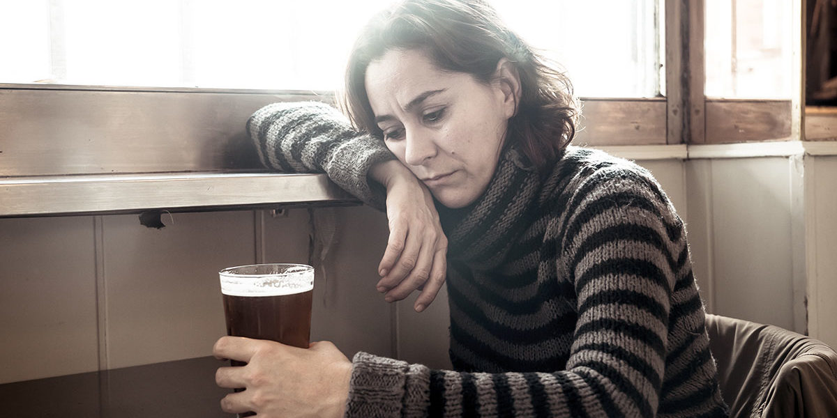 a woman stares at a beer and thinks about alcohol and depression