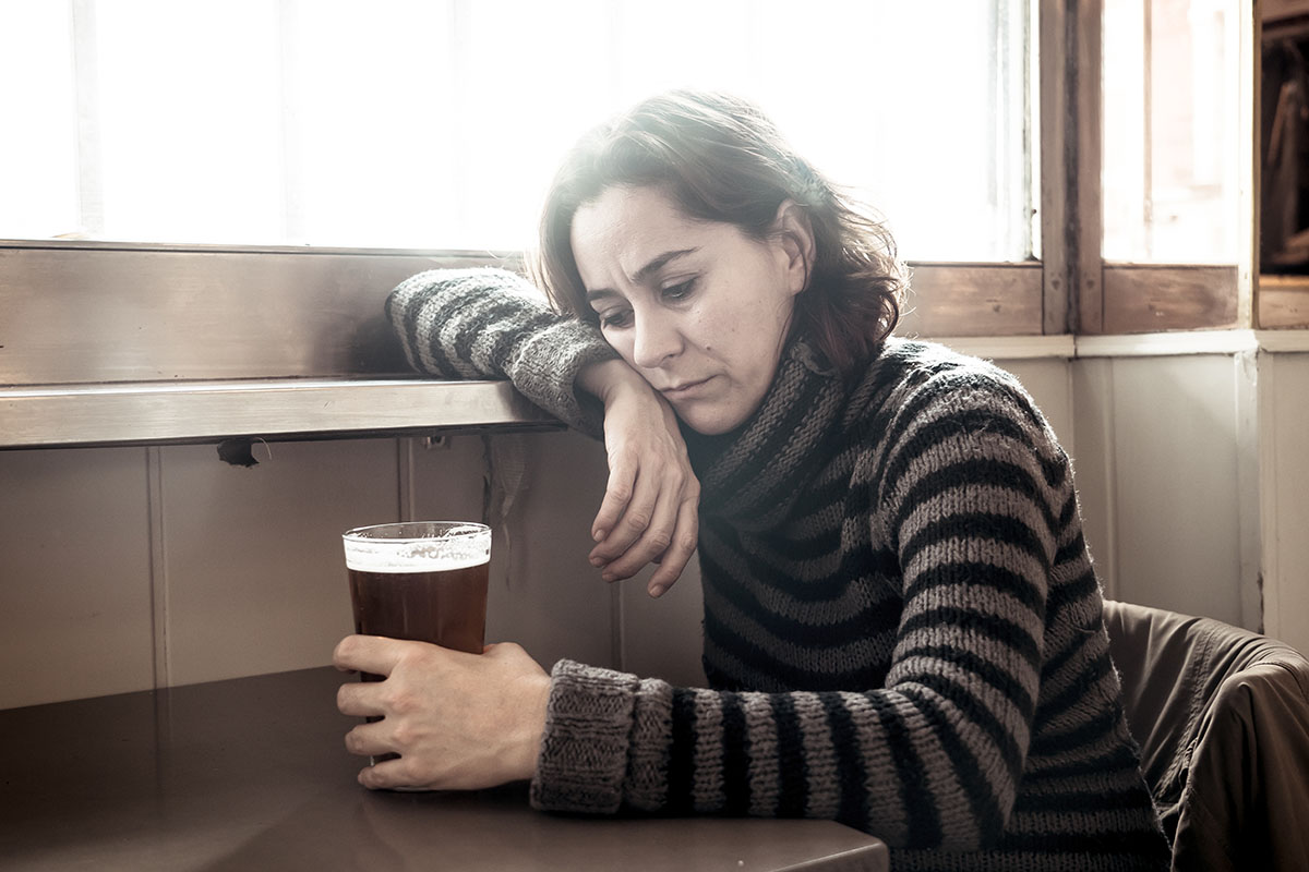 a woman stares at a beer and thinks about alcohol and depression