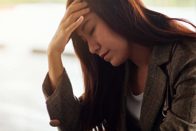 a woman puts her head in her hand as she struggles with anxiety and alcohol