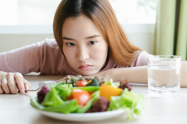 a woman stares at a salad and wonders about eating disorder causes