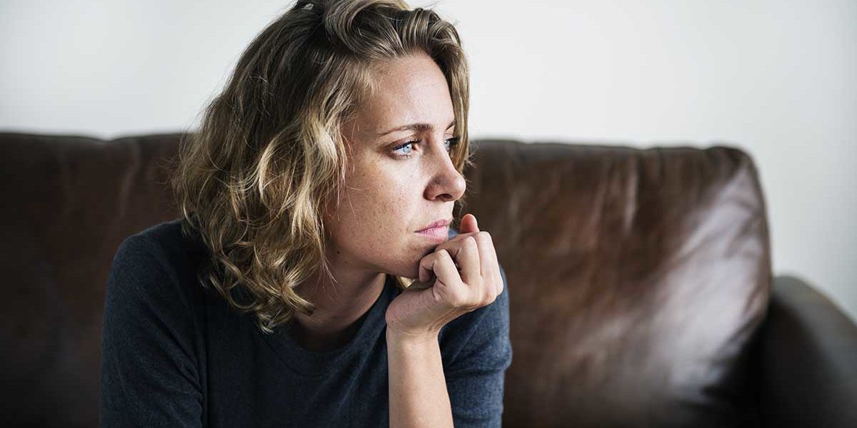 a woman sits on the couch as she considers the triggers of alcohol abuse