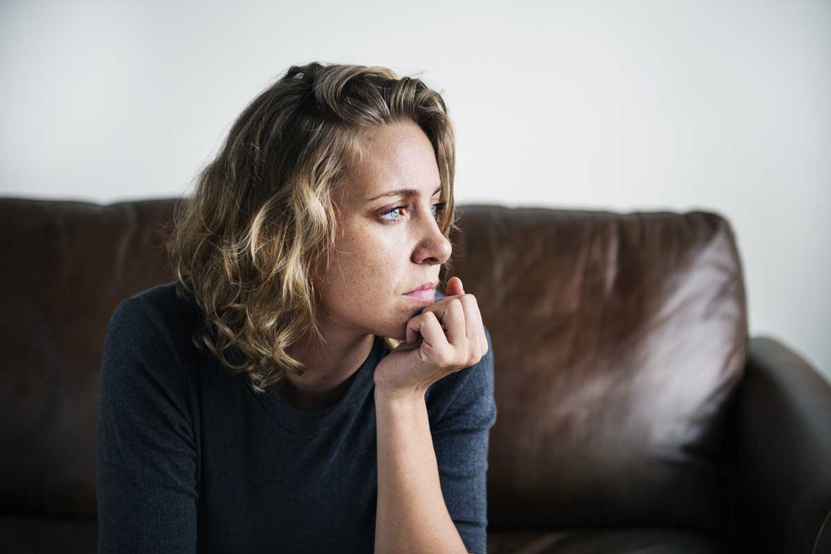 a woman sits on the couch as she considers the triggers of alcohol abuse