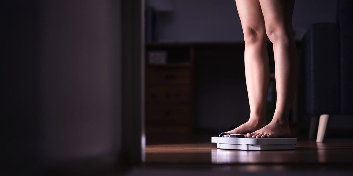 a woman stands on a scale and considers the connection between mental health and eating disorders