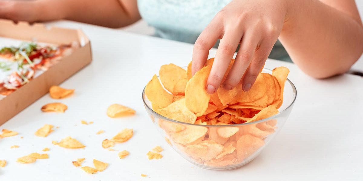 a woman wonders why she consider binge eating disorder treatment as she eats chips