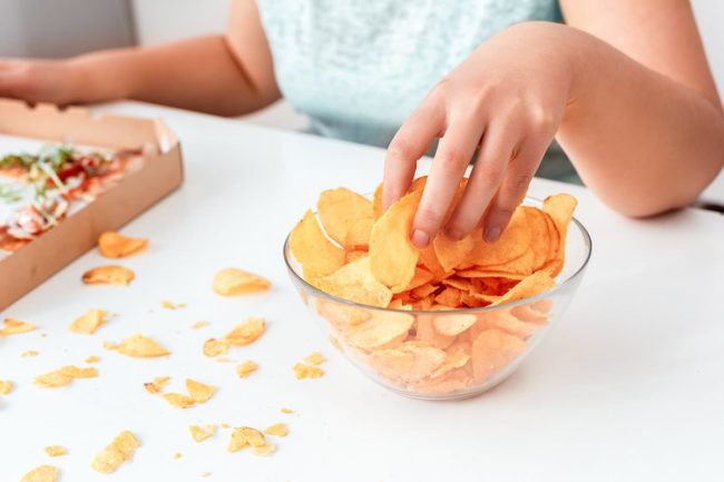 a woman wonders why she consider binge eating disorder treatment as she eats chips