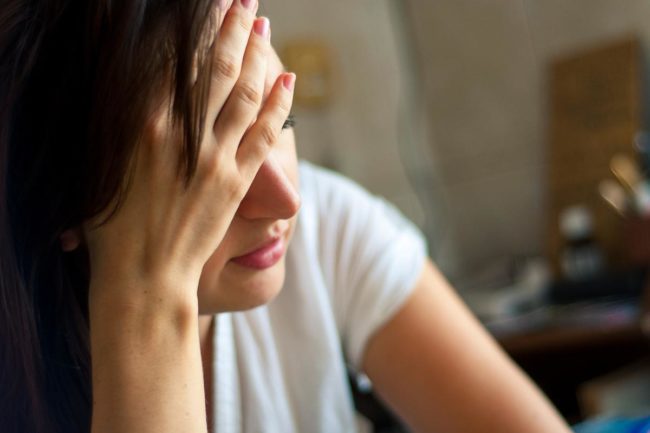 woman sitting with hand to her forehead learning about heroin addiction symptoms